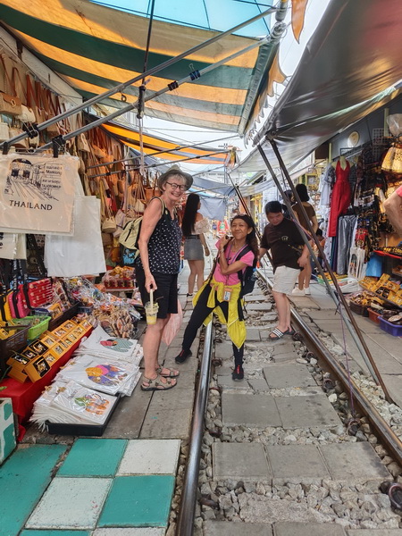 Tour guide and guest posing on the railway tracks at Maeklong Train Market surrounded by stalls