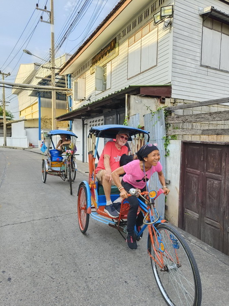 Guide pedaling a sam lor tricycle taxi with happy guests through Mahachai streets