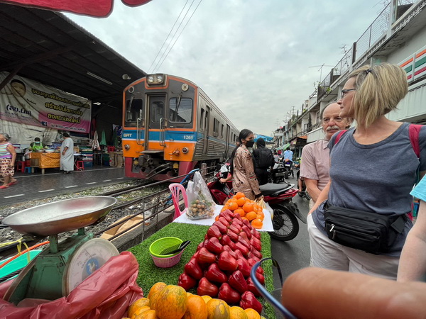 Train approaching through the Maeklong Railway Market with vendors and fresh produce on the tracks