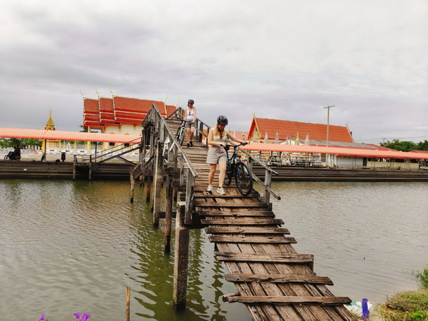 Cyclist carefully crossing a rustic ancient wooden bridge over water in Nakhon Pathom