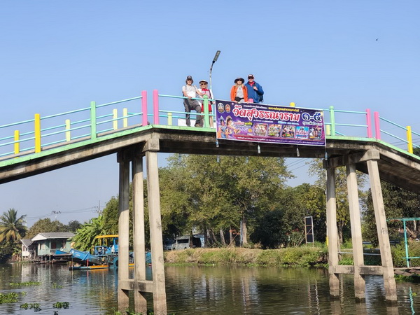Cyclists standing on a colorful bridge spanning a canal in Nakhon Pathom