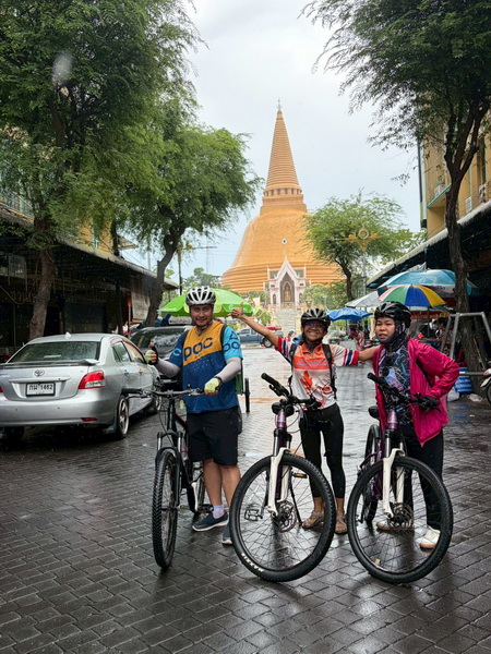 Group of cyclists posing with their bikes in front of Wat Phra Pathom Chedi on a rainy day