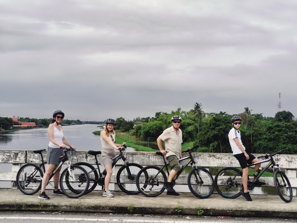 Cyclists posing with their bikes on a bridge overlooking the peaceful Ta Chin river