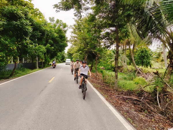 Cyclists riding along a quiet tree-lined rural road in the Nakhon Pathom countryside