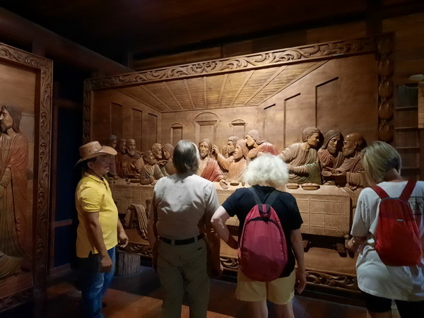 Guide explaining the intricate Last Supper wood carving to visitors at the Woodlands museum