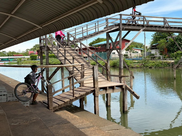 Cyclists navigating a steep old wooden bridge with bikes during the Nakhon Pathom tour
