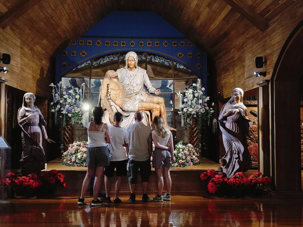 Family admiring an elaborate Christian-themed wood carving scene at the Woodlands museum