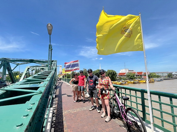 Cyclists crossing the Memorial Bridge over the Chao Phraya River with Thai flags