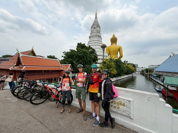 Cyclists posing on a bridge over the main canal with Wat Paknam in the background