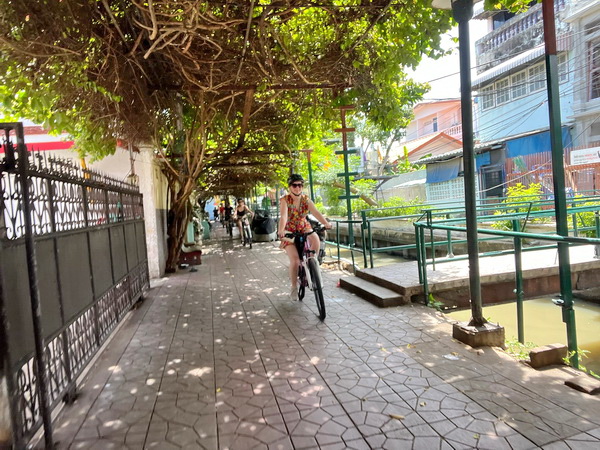 Cyclist riding along a shaded canal path on the way to Wat Paknam