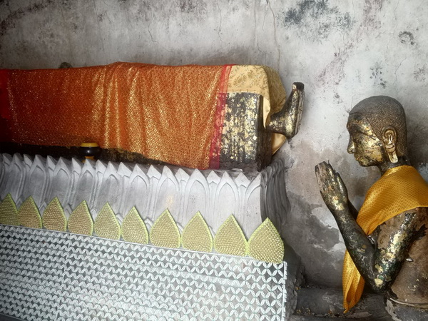 Ancient Buddha image in a coffin with praying monk statues at Wat Paknam