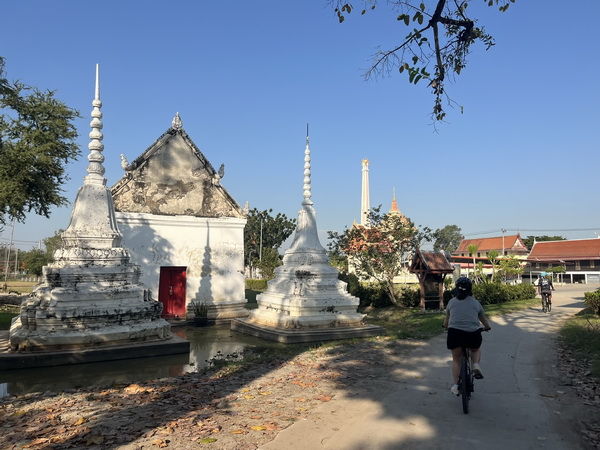 Cyclist riding past traditional white stupas and temples in a quiet riverside village