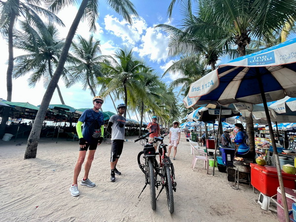 Tour group with bikes at Bang Saen beach final destination among palm trees and beach umbrellas