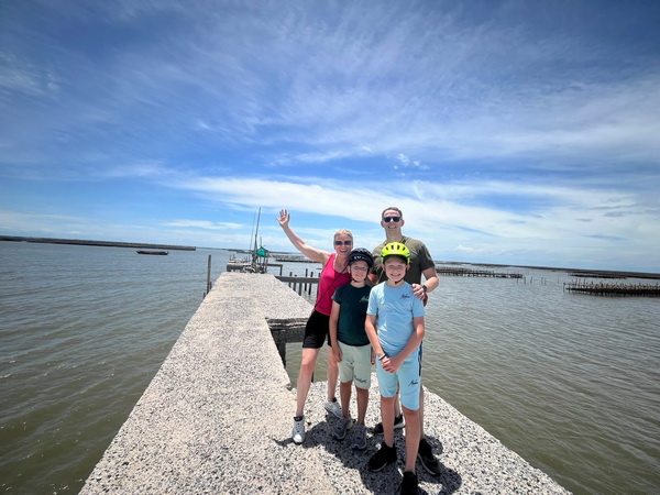 Family posing on a concrete pier with oyster farms and blue sky in the background