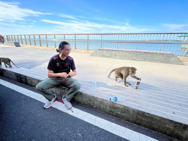 Playful monkey stealing a water bottle from a tour guest at Khao Sam Muk
