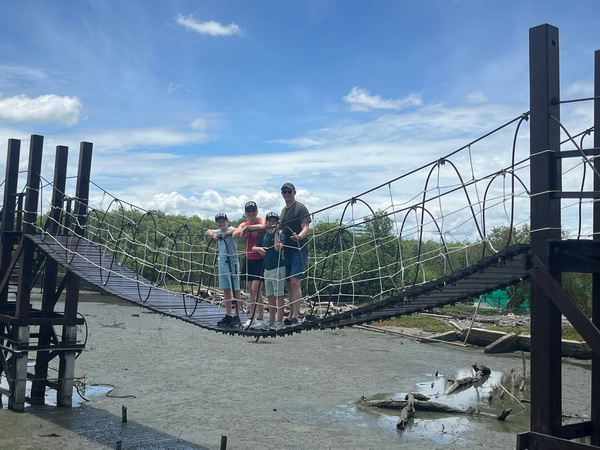 Family standing on a rope bridge over the mangrove estuary at Bang Saen