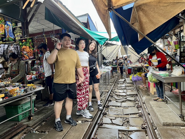 Tour guests walking through the Maeklong train market on the railway tracks before the train arrives