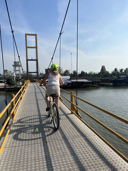 Cyclist riding over a beautiful yellow suspension bridge on the floating market bike tour