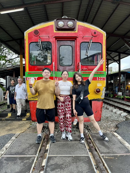Tour guests posing in front of a colorful train at the Maeklong railway station