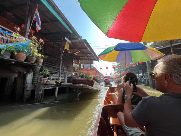 Tourists on a boat ride through the vibrant Damnoen Saduak floating market with colorful umbrellas
