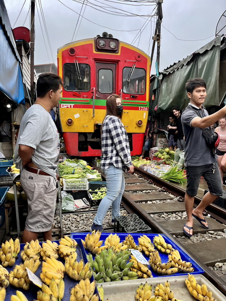 Red and yellow train passing directly through the Maeklong Railway Market with banana stalls on the tracks