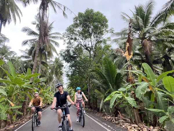 Cyclists enjoying a peaceful ride through lush coconut plantations on the floating market tour