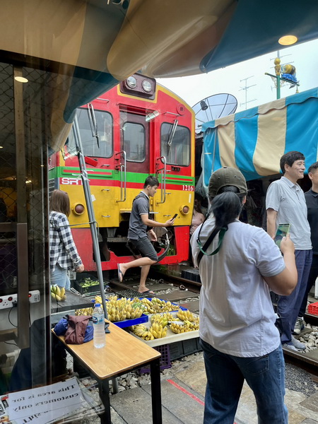 Train passing through the Maeklong Railway Market with vendors and shoppers nearby