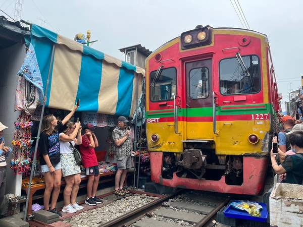Colorful red and yellow train coming through the Maeklong market with tourists taking photos