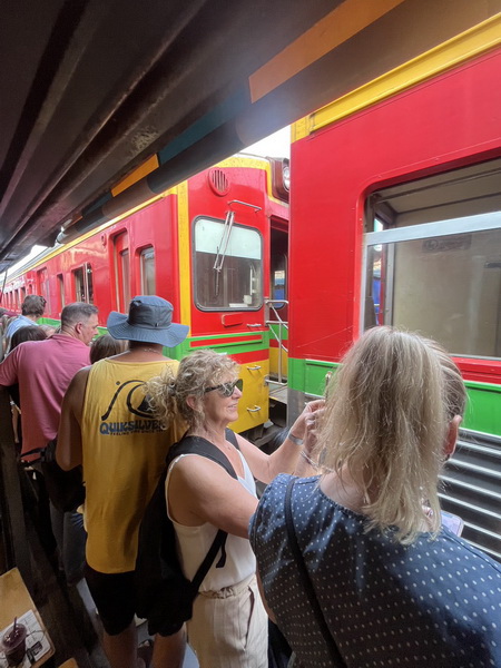 Tourists standing very close to the train as it passes through the narrow Maeklong Railway Market