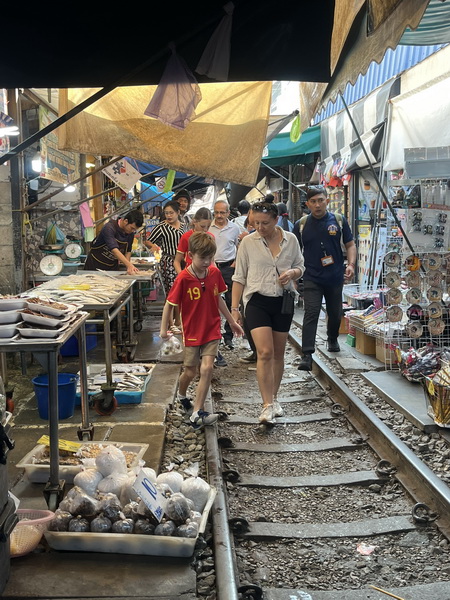 Tour guests walking through the Maeklong train market stalls set up on the railway tracks