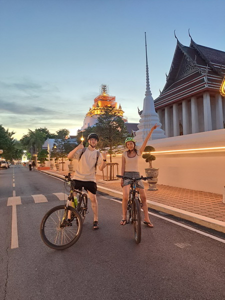 Two cyclists posing on the street with the illuminated Golden Mountain temple glowing in the twilight background