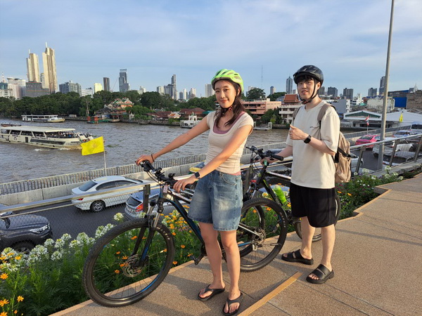 Cyclists posing with their bikes on the modern Sky Garden bridge with Bangkok skyline in background