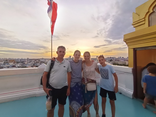 Family posing for a group photo on Golden Mountain with a beautiful golden sunset and Bangkok skyline behind them