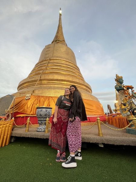 Two friends posing in front of the magnificent golden chedi at the top of Golden Mountain temple
