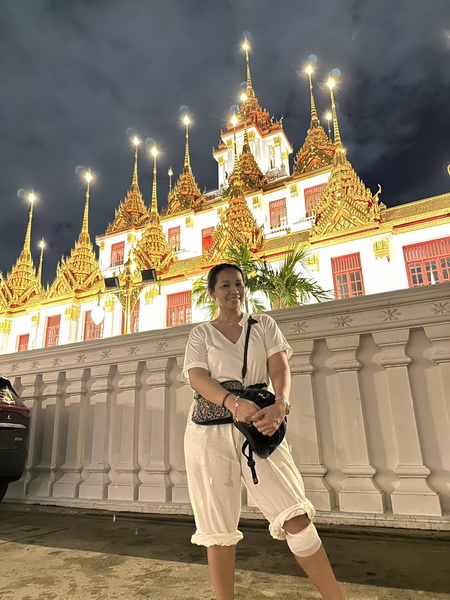 Visitor posing in front of the stunning Loha Prasat Iron Roof Temple beautifully illuminated at night