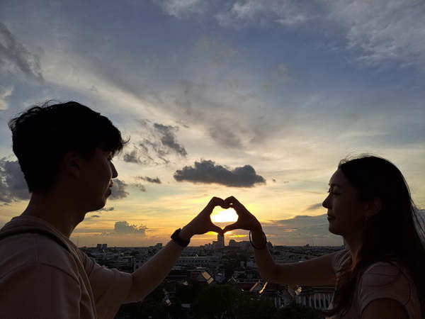 Romantic couple making a heart shape with their hands framing the setting sun over Bangkok skyline