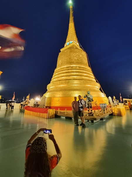Couple posing for a photo at the illuminated Golden Mountain chedi after dark with city lights in background