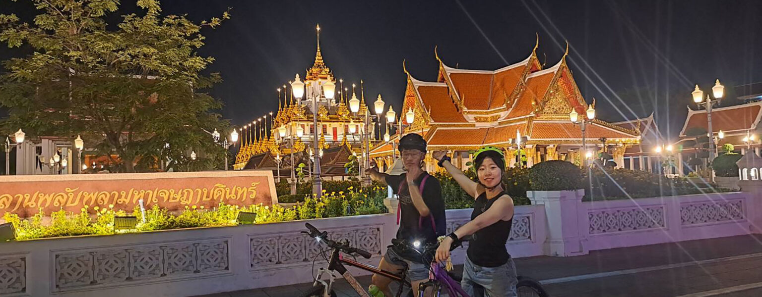 Bangkok city skyline illuminated at night with cyclists exploring temples and streets by bicycle