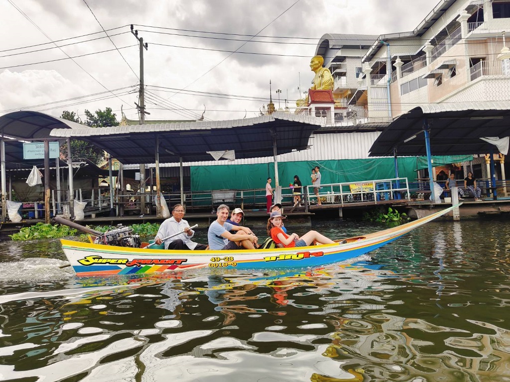 Long tail boat riding through Bangkok canals with stilted houses and lush greenery